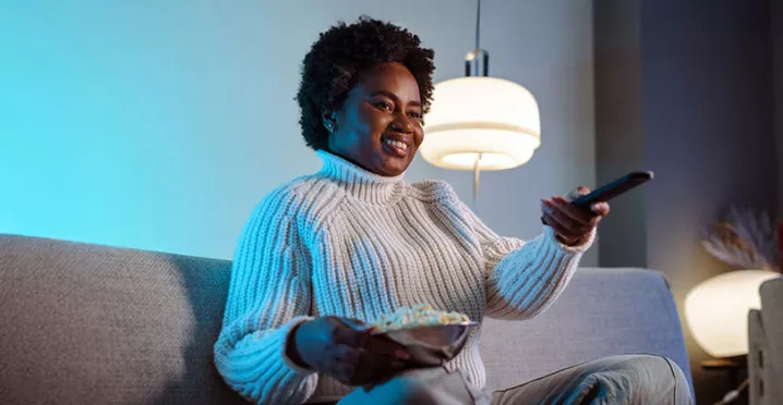 mulher em sofá segurando um balde de pipoca e controle remoto.