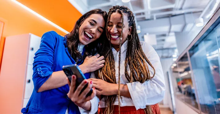 duas mulheres rindo enquanto olham algo em celular.