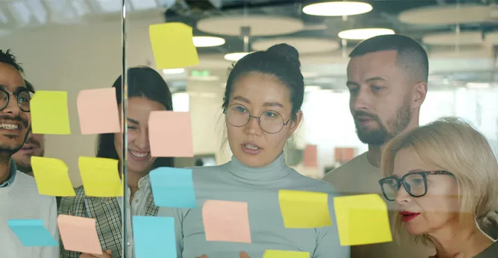 grupo de pessoas olhando para notas autoadesivas em parede de vidro.