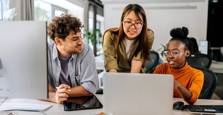 três pessoas conversando enquanto olham algo em computador.