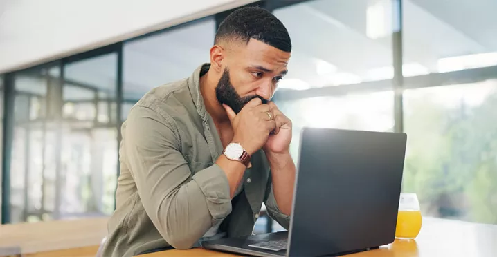 Foto mostra um homem preocupado olhando para seu notebook no escritório