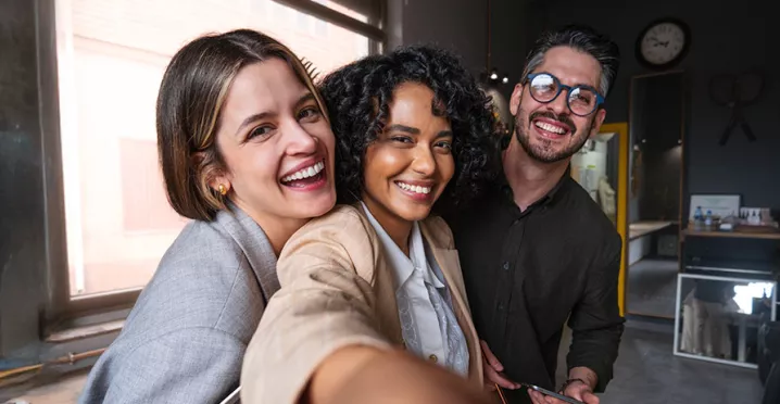Foto mostra três colegas de trabalho tirando uma selfie no escritório