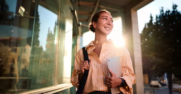 Foto de uma jovem profissional na área externa da empresa em que trabalha