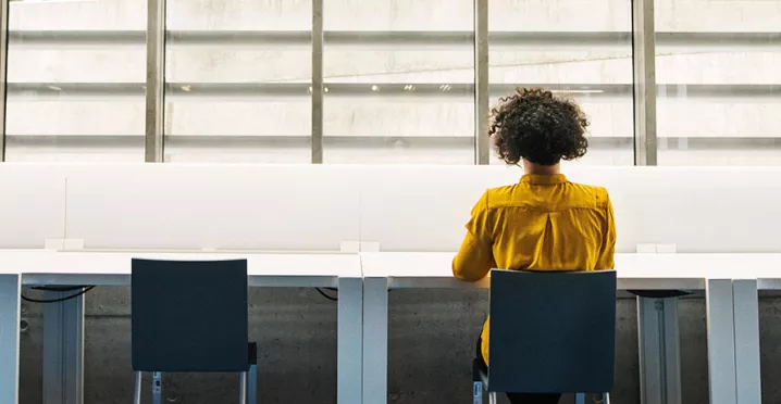 mulher trabalhando sozinha em mesa cheia de cadeiras.