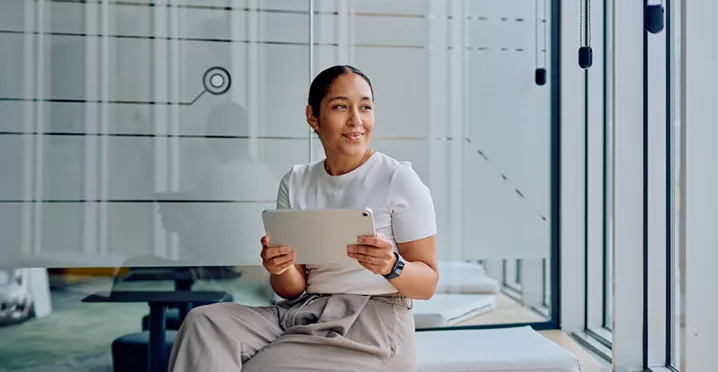 mulher segurando tablet e olhando pela janela em escritório.