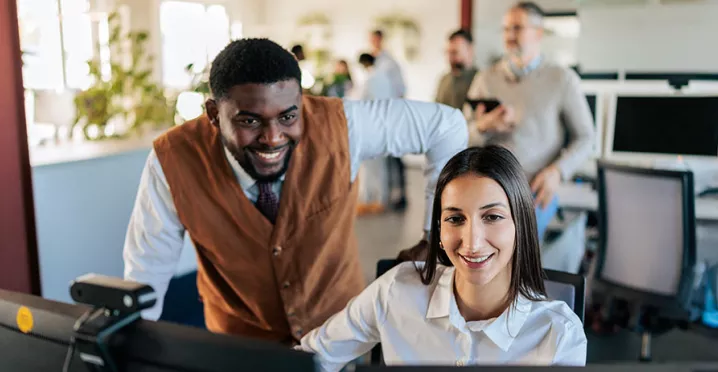 um homem e uma mulher sorrindo olhando para computador em escritório.