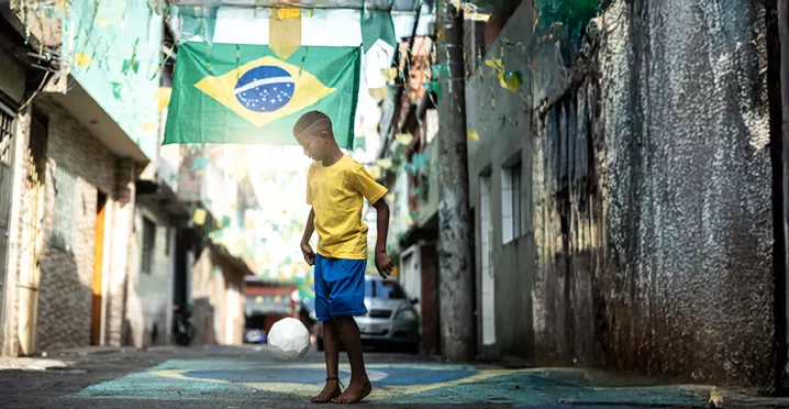 Foto mostra um menino jogando bola em uma rua enfeitada para a Copa do Mundo