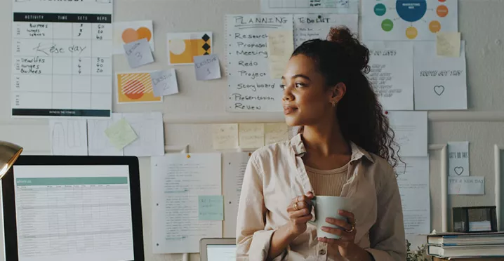 mulher segurando xícara de café em frente a uma série de papéis com planejamento estratégico.