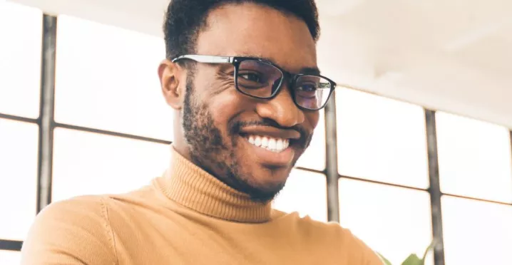 Homem negro, de camiseta amarela olhando para o notebook e sorrindo
