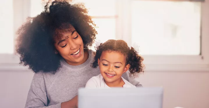 mãe e filha sorrindo enquanto olham algo no computador.