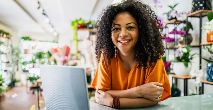 dona de floricultura sorrindo com computador.