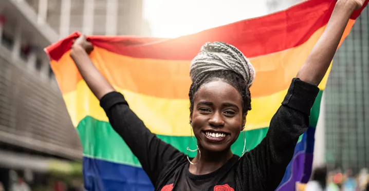 mulher sorrindo enquanto segura uma bandeira LGBT.