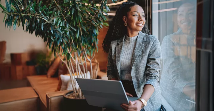 mulher empreendedora olhando pela janela sorrindo com notebook no colo.