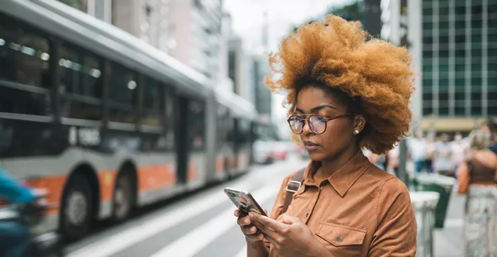 mulher usando o celular enquanto onibus do sistema de transporte de são paulo passa ao lado.
