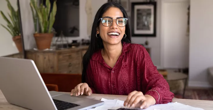 mulher sorrindo enquanto vê algo em notebook.