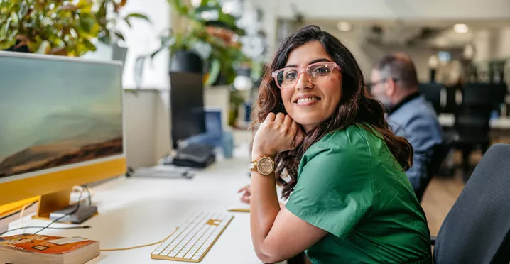 mulher sorrindo para a câmera enquanto trabalha em frente a computador.