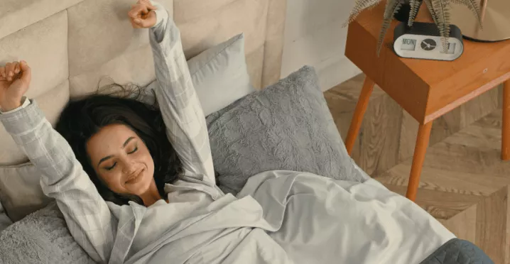 A imagem mostra uma mulher em uma cama, se espreguiçando ao acordar 