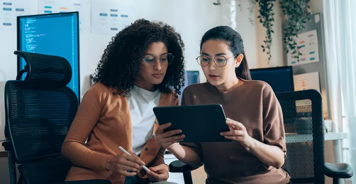 duas mulheres discutindo sobre algo enquanto olham tablet.