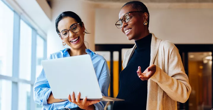 duas mulheres conversando animadamente enquanto veem algo em computador.