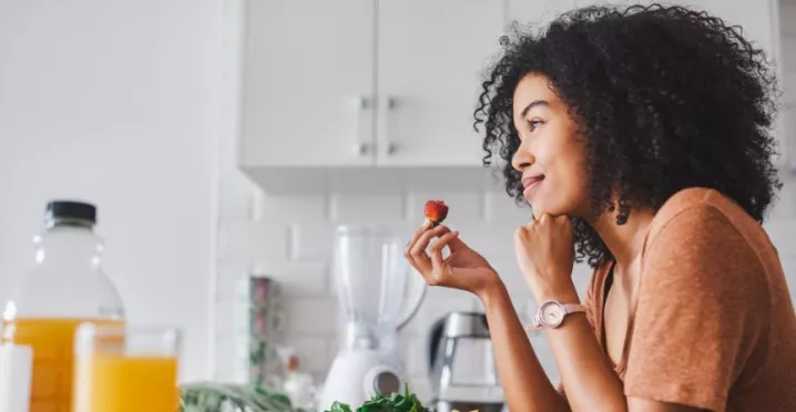 mulher olhando pela janela com um morango na mão 