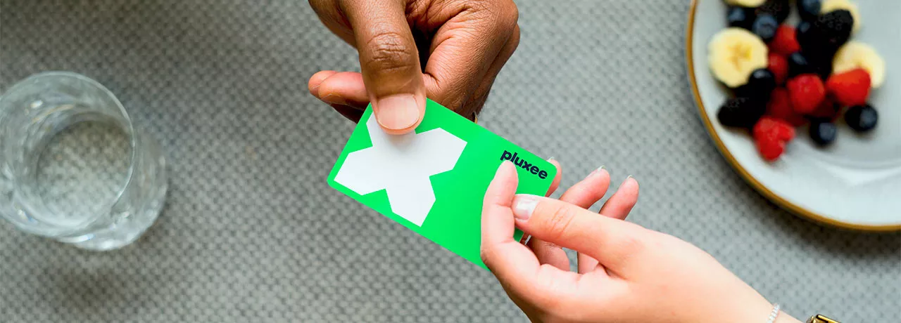 Mulher usa o cartão de benefício Pluxee para pagar uma conta. Nossos cartões são feitos com plástico reciclável!