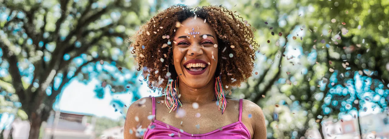 Foto mostra mulher sorridente pulando Carnaval numa praça