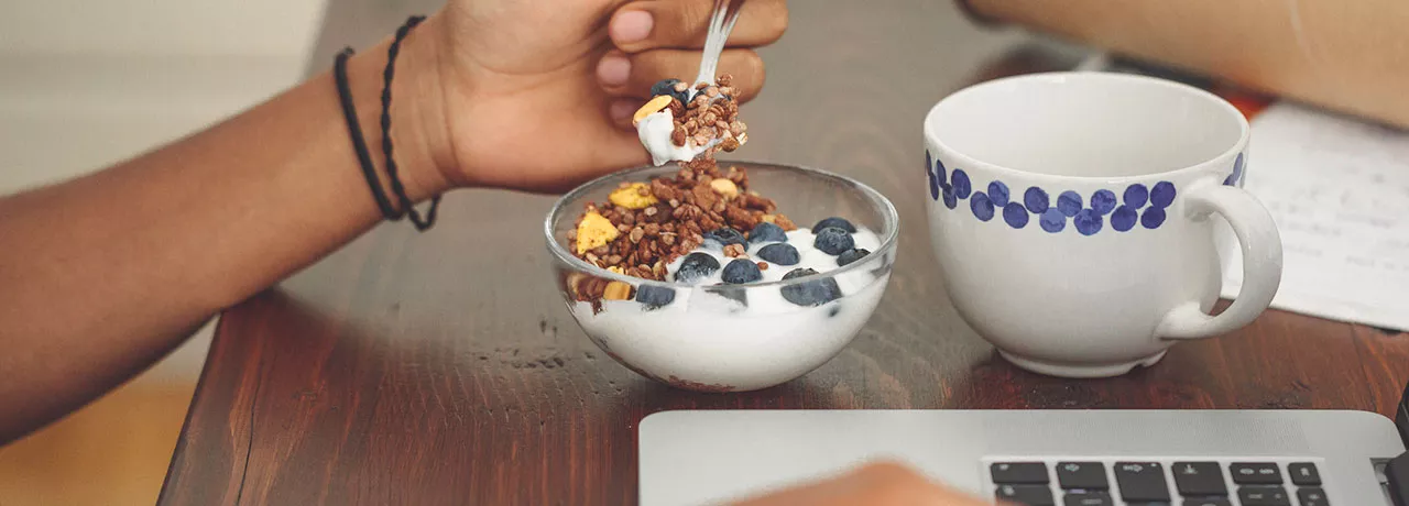 Foto mostra uma tigela de iogurte que uma pessoa está comendo durante o trabalho
