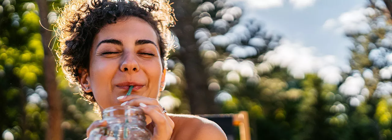 Foto mostra mulher tomando um suco em um parque