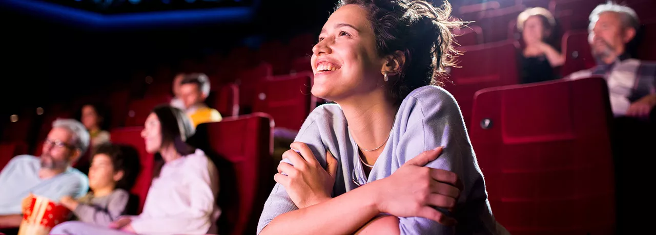 Mulher sorri e assiste com atenção a um filme no cinema