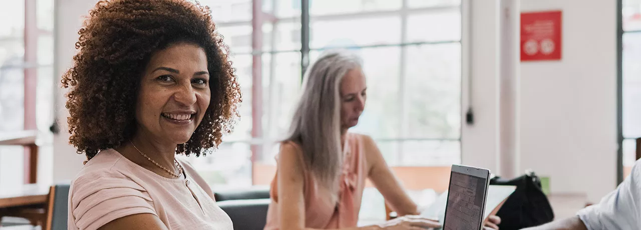 Mulher sorri para a câmera em um ambiente de trabalho com diversidade e inclusão