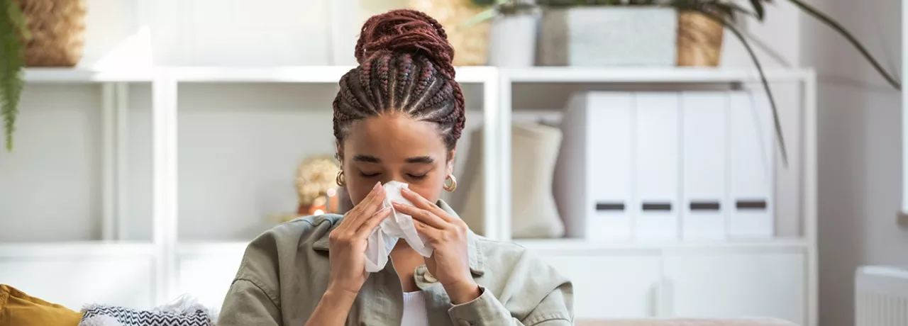 Foto mostra uma mulher assoando o nariz porque está resfriada 