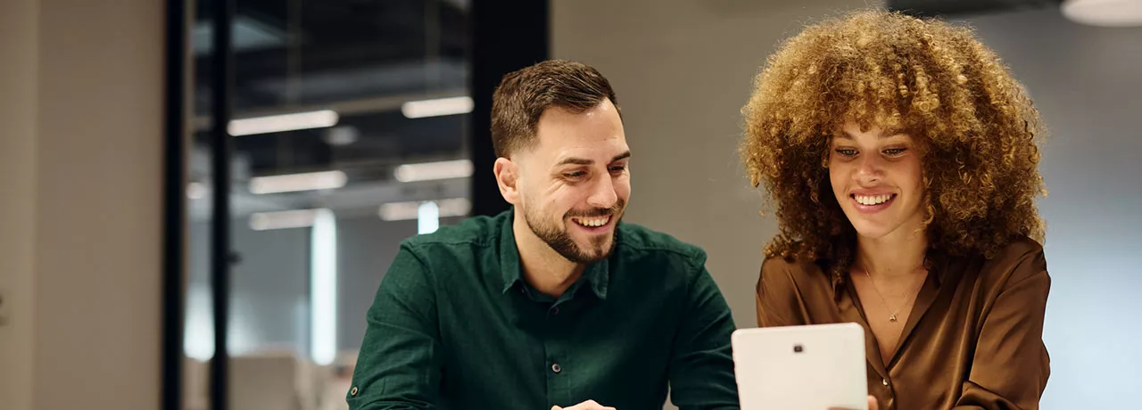 um homem e uma mulher sorrindo olhando para tablet.