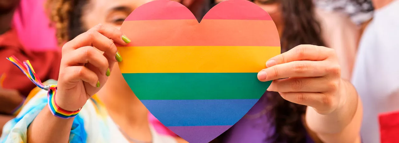 Foto mostra duas pessoas segurando um coração de arco-íris