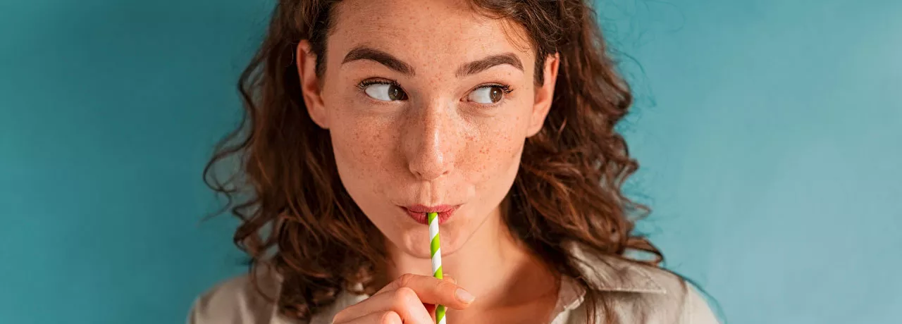 Foto mostra uma mulher tomando uma bebida de canudinho