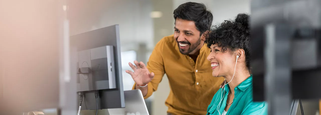 duas pessoas conversando e sorrindo em frente a um computador.