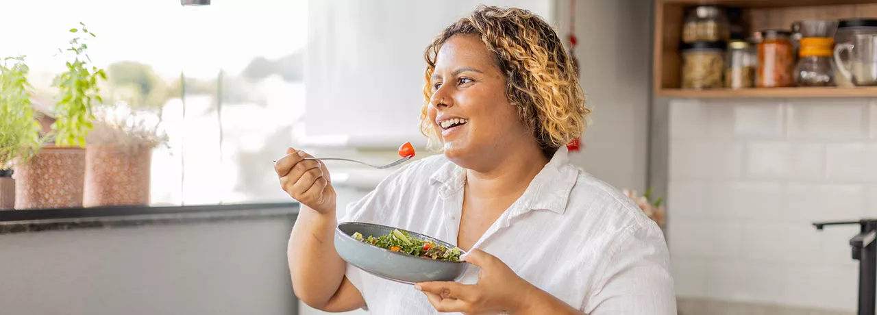 mulher comendo salada sorrindo.