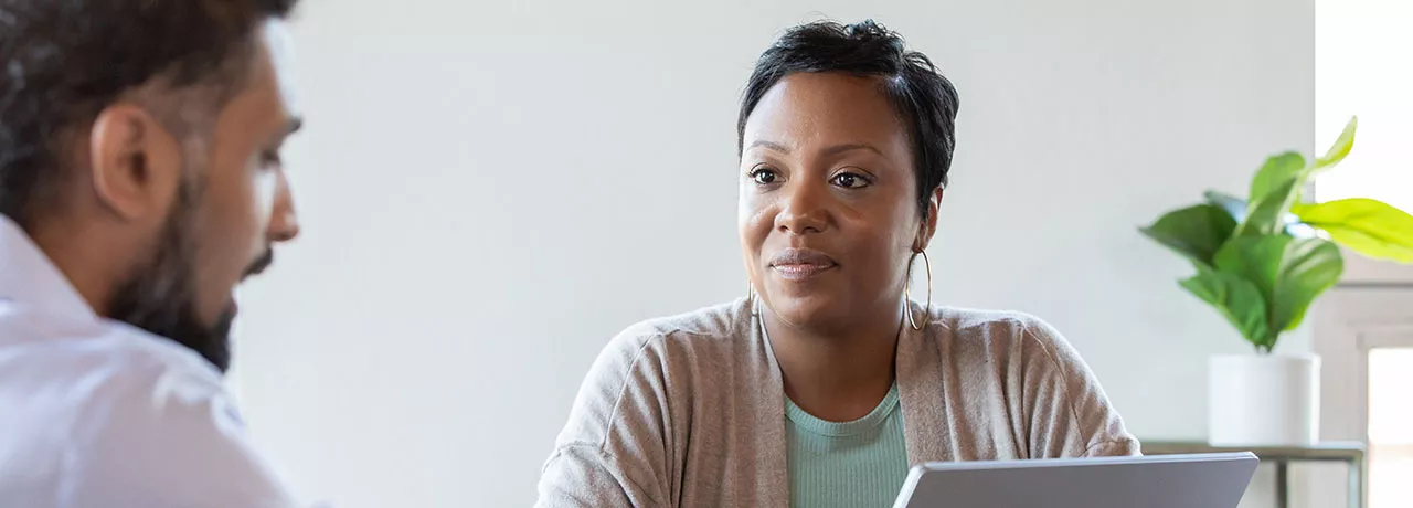homem conversando com mulher que senta atrás de um notebook.
