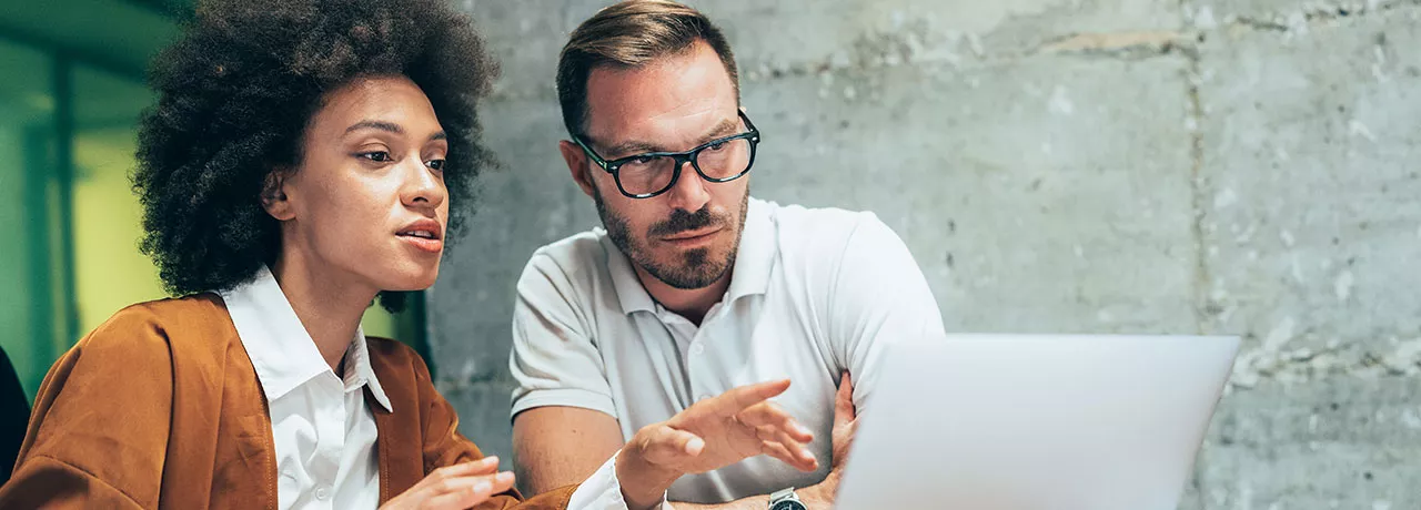 duas pessoas conversando sobre algo enquanto apontam para a tela do notebook.