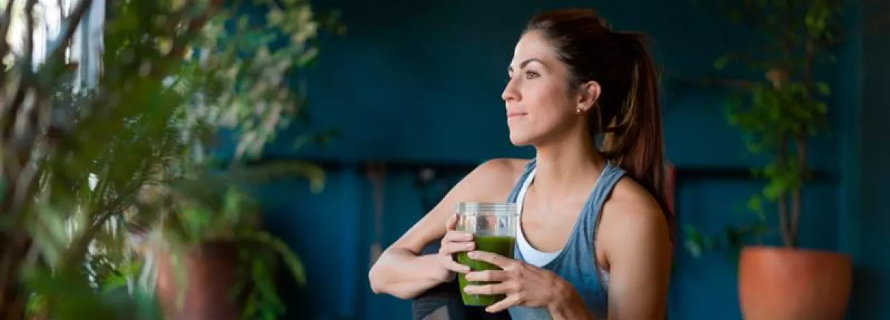 Imagem mostra uma mulher branca tomando um suco verde 