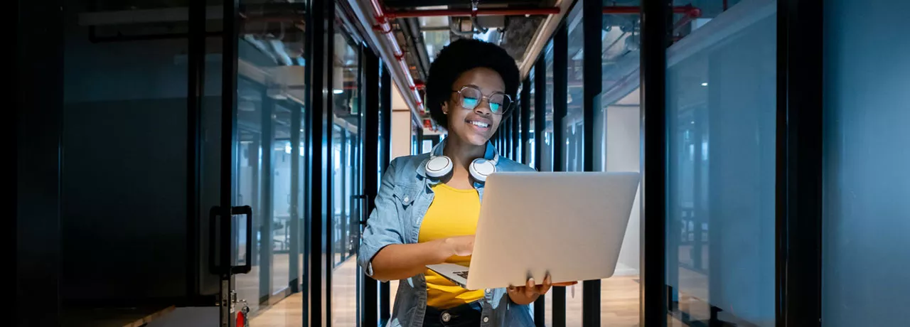mulher sorrindo enquanto segura computador e caminha em um corredor de escritório.