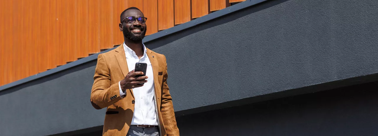 homem "CLT premium" feliz andando na rua enquanto segura o celular.