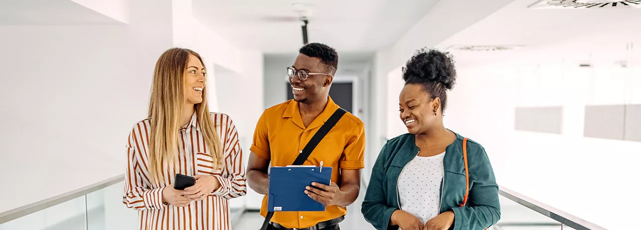 três pessoas conversando e rindo em corredor.