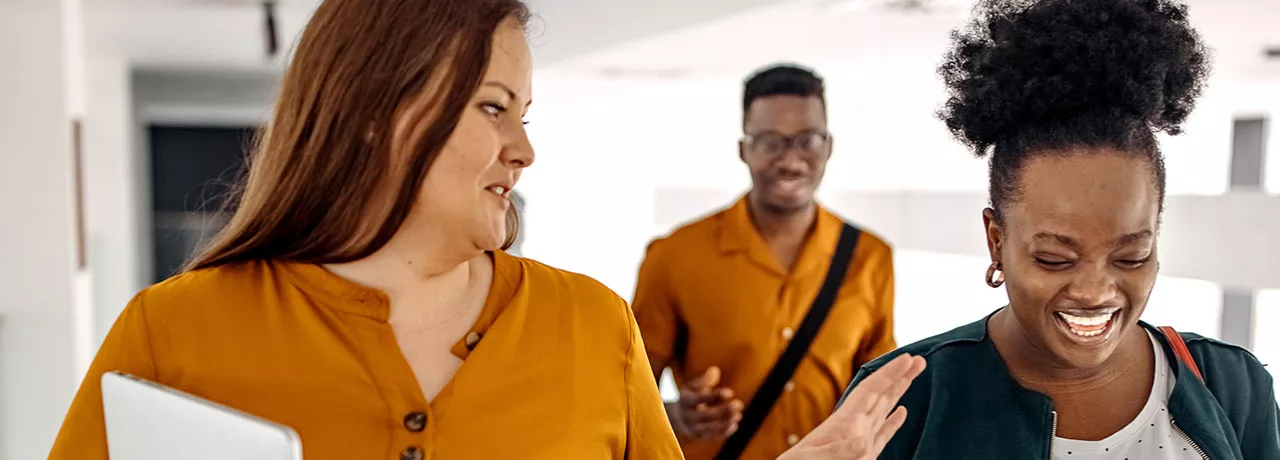 três pessoas conversando e rindo em corredor.