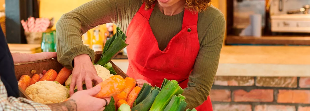 foto mostra duas pessoas mexendo em uma cesta de legumes frescos