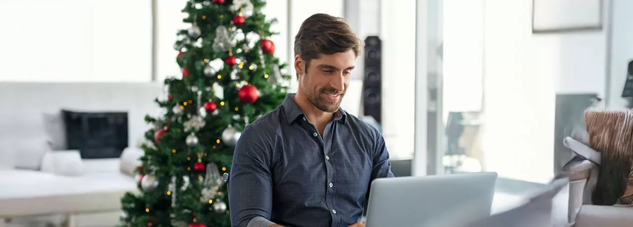 homeme trabalhando com árvore de natal atrás.