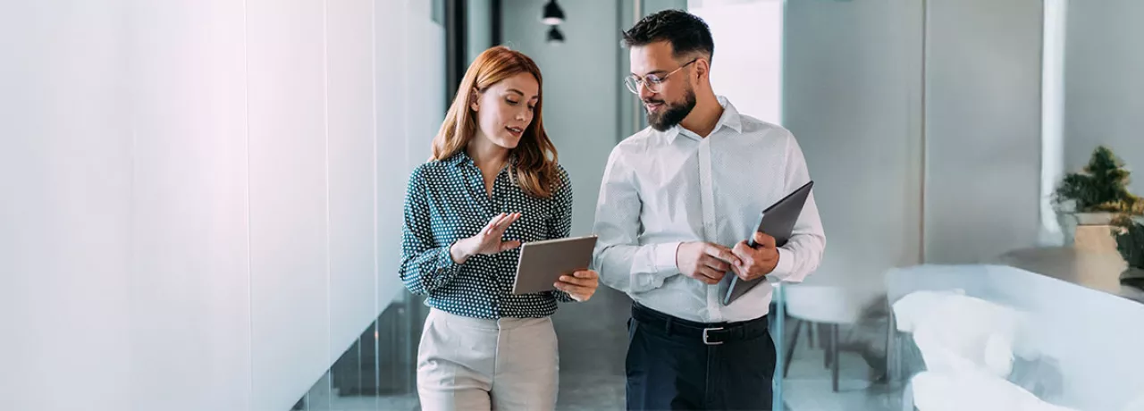 duas pessoas conversando enquanto olham dado em tablet dentro de uma empresa.