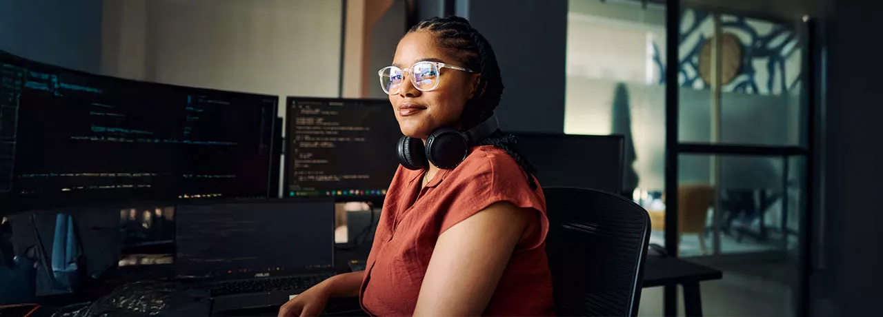 mulher sentada olhando para a câmera com monitores ao fundo.