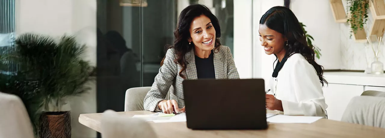 duas mulheres sorrindo enquanto conversam em frente a um notebook no escritório.