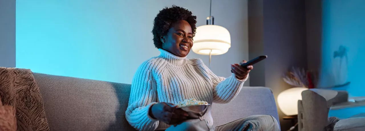 mulher em sofá segurando um balde de pipoca e controle remoto.