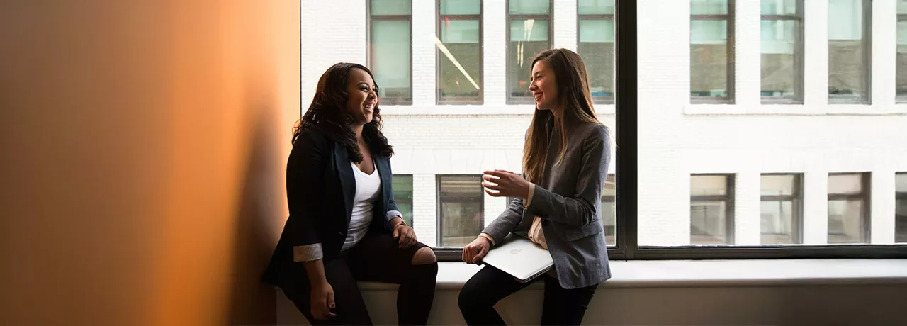 Foto mostra duas pessoas conversando em uma sala de reunião
